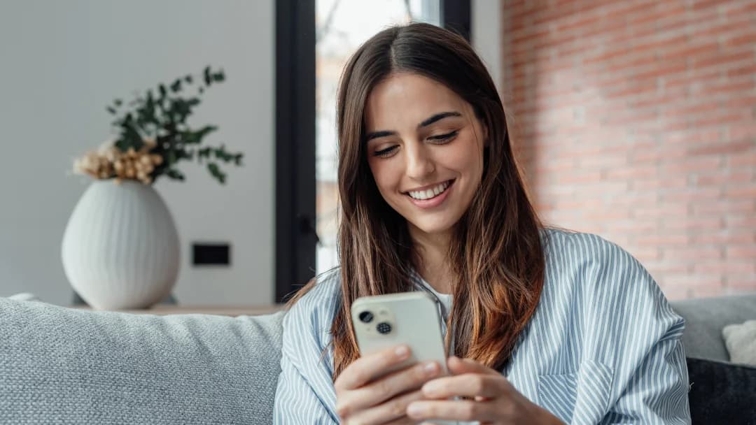 Une femme souriante utilisant son téléphone, illustrant la facilité d'accès aux prêts sans vérification de crédit.