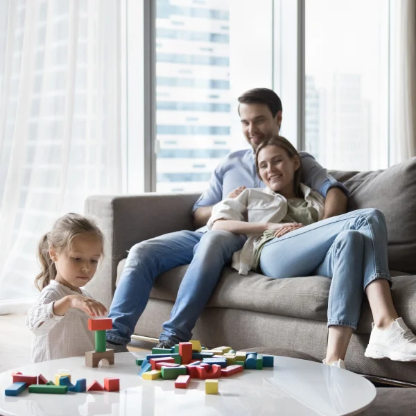 Une famille assise sur un canapé, un enfant jouant avec des blocs de construction. Atmosphère chaleureuse et conviviale.