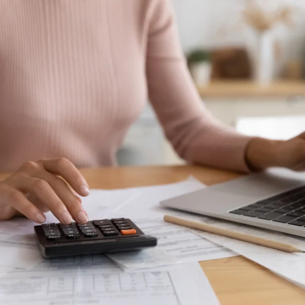 Femme utilisant une calculatrice et un ordinateur portable à domicile, analysant des informations sur les hypothèques privées.