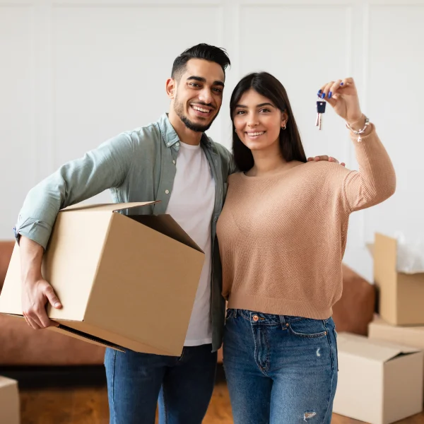 Un jeune couple tenant une clé et déplaçant des cartons, symbolisant l'achat d'une maison avec des hypothèques privées.