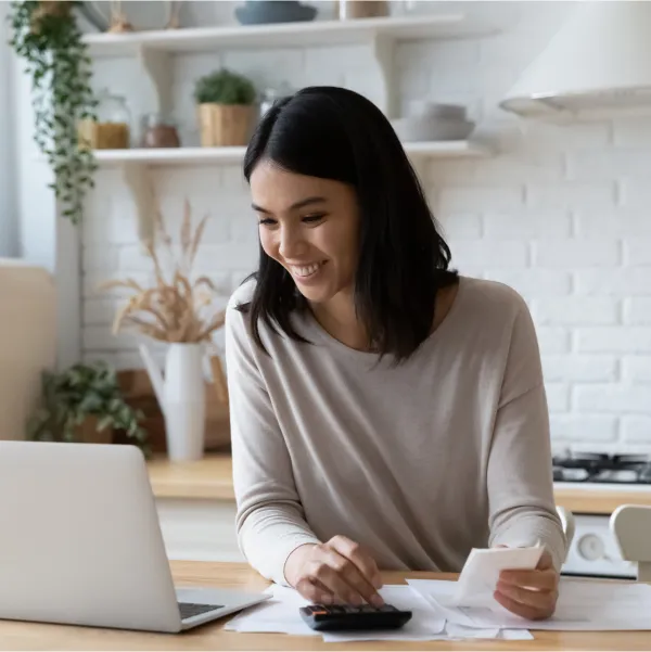 Femme utilisant son ordinateur portable et sa calculatrice dans sa cuisine, prête avec un mauvais crédit.